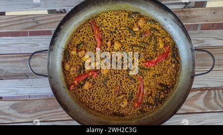 Reis in einer Paella-Pfanne auf einem rustikalen Holztisch mit Blick von oben zubereitet Stockfoto