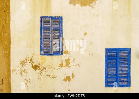 Blick auf blaue Fenster und Fensterläden an einer alten Hauswand mit weißer Farbe. Essaouira (Mogador), Marokko Stockfoto
