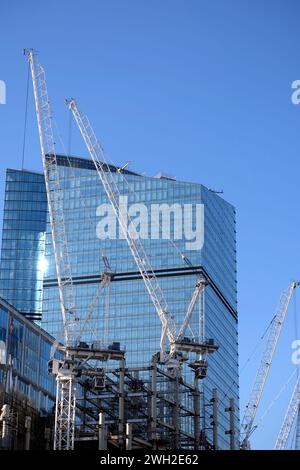 Mehrere Turmkräne bauen einen modernen hohen Wolkenkratzer vor einem klaren blauen wolkenlosen Himmel Stockfoto