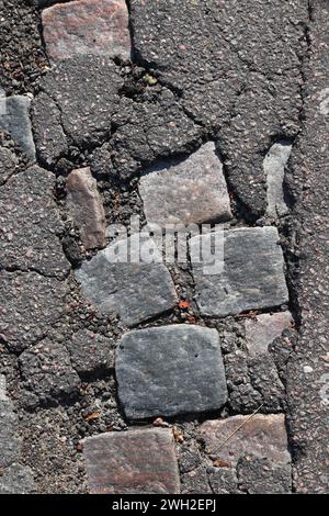 Beschädigte Straßenoberfläche in Göteborg, Schweden. Historisches Kopfsteinpflaster unter moderner Asphaltdecke. Stockfoto