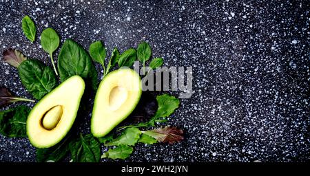 Zusammensetzung von halbierter Avocado und frischem Blattgemüse - Grundlagen einer gesunden pflanzlichen Ernährung. Extra breites Banner. Stockfoto