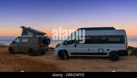 Santa Pola, Spanien - 4. Februar 2024: Zwei Wohnmobile parken auf einem Sandparkplatz neben dem Strand bei Sonnenuntergang Stockfoto