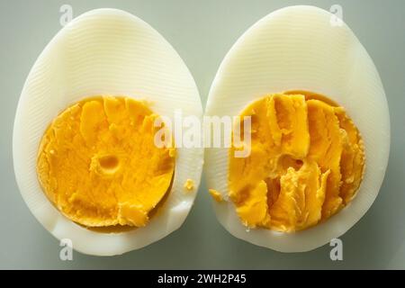 Nahaufnahme eines in zwei Hälften geschnittenen Eies auf weißgrauem Hintergrund. Stockfoto