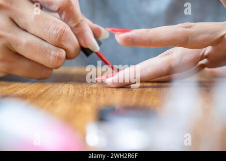 Nahaufnahme von Frauenhänden, die ihre Nägel rot färben. Stockfoto