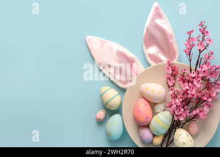 Frohe Ostern. Bunte ostereier und rosa Mandelblüten auf einem Teller mit Platz für Text auf blauem Hintergrund Stockfoto