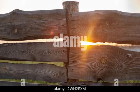 Sonnenlicht scheint durch den hölzernen rustikalen Zaun in einem wunderschönen Abendsonnenverlauf. Stockfoto