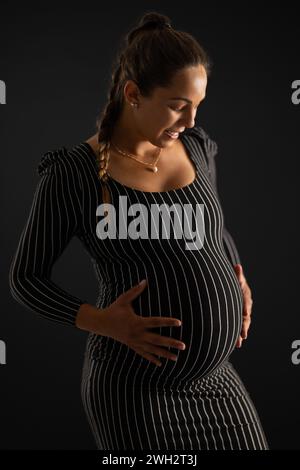 Lächelnde Schwangere in gestreiftem Kleid mit schwarzem Hintergrund Stockfoto