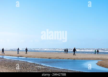 Egmond aan Zee, Niederlande - 17. März 2022: Breiter Sandstrand in der Sonne mit einigen Menschen entlang eines rauen Meeres Stockfoto