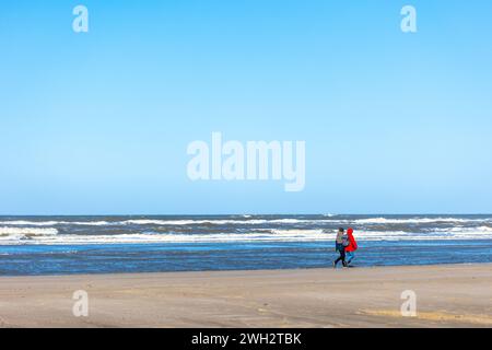 Egmond aan Zee, Niederlande - 17. März 2022: Breiter Sandstrand in der Sonne mit zwei Personen entlang eines rauen Meeres Stockfoto