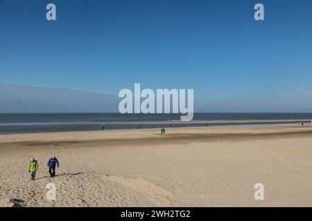 Egmond aan Zee, Niederlande - 16. März 2022: Breiter Sandstrand in der Sonne, nur wenige Leute spazieren gehen Stockfoto