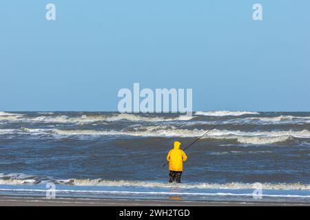 Egmond aan Zee, Niederlande - 17. März 2022: Ein Fischer mit einem gelben Cagoule im rauen Meer der Nordsee in der Nähe des Strandes Stockfoto