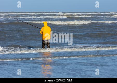 Egmond aan Zee, Niederlande - 17. März 2022: Ein Fischer mit einem gelben Cagoule im rauen Meer der Nordsee in der Nähe des Strandes Stockfoto