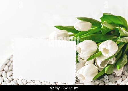 Blumenstrauß aus frischen weißen Tulpen und unbeschrifteter Karte am Muttertag oder Frauentag. Draufsicht mit Kopierraum Blumenkomposition romantischer Hintergrund Stockfoto