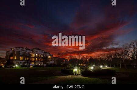 Park mit Lichtern bei Sonnenuntergang und feurig rotem Himmel. Nachtsicht in Landschaftsausrichtung mit Gebäuden und Bäumen dahinter. Stockfoto