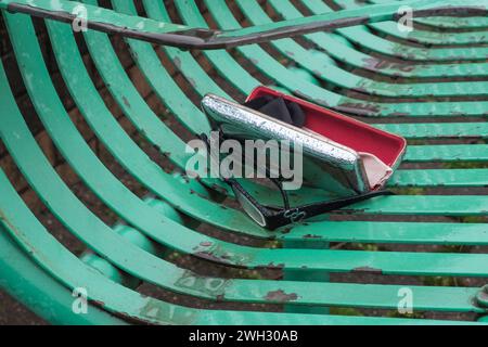 Brille oder Brille und Tasche, verloren auf einer Parkbank aus Metall Stockfoto