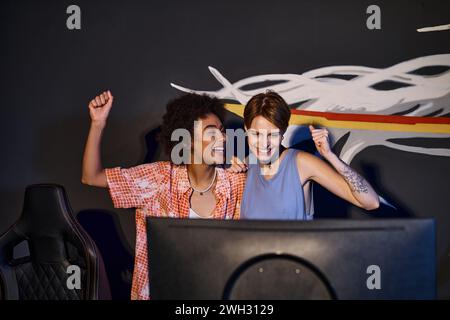 Multikulturelle glückliche Freundinnen, die auf Computermonitor schauen und den Sieg feiern, Cybersport Stockfoto