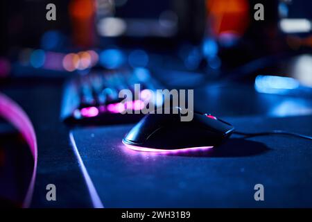Nahaufnahme einer beleuchteten Computermaus in der Nähe von Computertastatur, Cybersport und Gaming-Zubehör Stockfoto