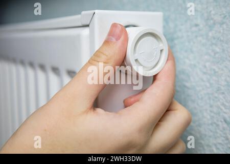 Frau regelt die Heizung auf weißem Batterieheizkörper zu Hause in der kalten Wintersaison, Hände in Nahaufnahme. Zentralheizung in einem gepflegten modernen Gebäude. A Stockfoto