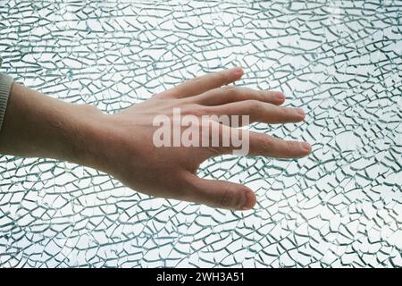 Nahaufnahme einer Hand, die gegen ein Glasgewebe gedrückt wurde. Der Mann berührt das zerrissene Glas mit seiner Hand Stockfoto