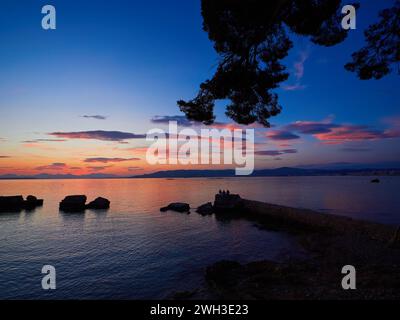 Bewölkter Sonnenuntergang über der Bucht von Cannes, Frankreich, mit Menschen auf den Felsen, die vor dem ruhigen rosa Meer stehen. Stockfoto