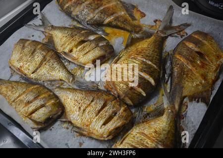 Köstlicher und gesunder, gebackener Fisch, Carassius mit Zitrone auf einem schwarzen Backblech mit weißem Pergamentpapier. Stockfoto