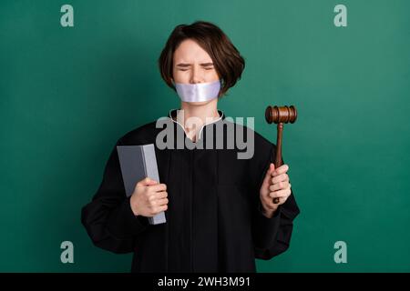 Foto einer jungen verängstigten Frau Richterin mit geschlossenen Augen Hammer falsches Urteil isoliert auf grünem Hintergrund Stockfoto