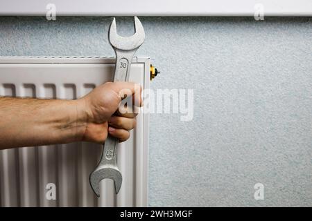 Ein Mann montiert einen Heizkörper an der Wand. Das Konzept der Hausrenovierung. Heizungsabschaltung, Wärmeprobleme Stockfoto