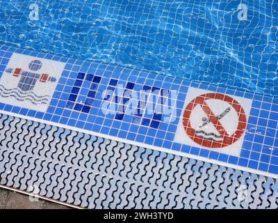 Ein Blick auf den Poolrand mit spezifizierter Tiefe für sicheres Schwimmen und ein Warnschild, das Tauchen verbietet. Spanien. Stockfoto