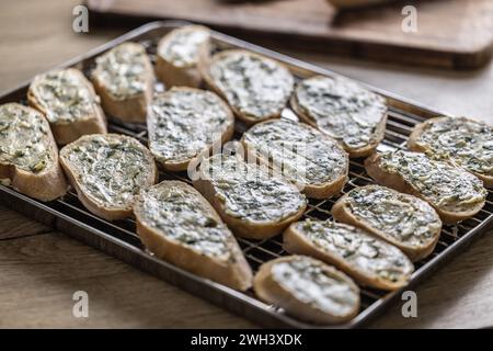 Mini-Baguettes mit Kräuter-Knoblauchbutter, fertig zum Backen auf einem Tablett. Stockfoto