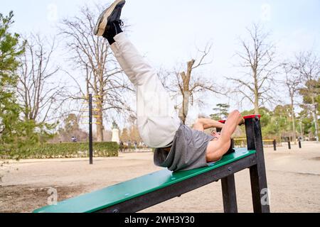 Junger männlicher Athlet, der Sit-ups macht, indem er seine Beine in einem Outdoor-Calisthenics-Park hebt Stockfoto