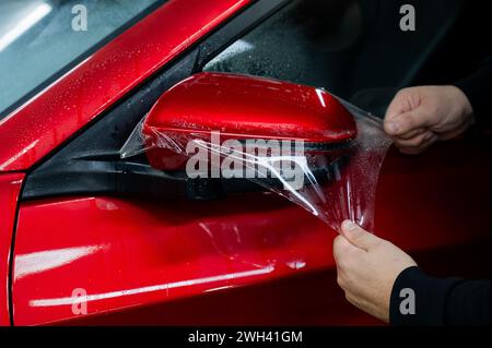 Der Master trägt Vinylfolie auf den Seitenspiegel eines Autos auf. Stockfoto