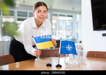 Geschäftsfrau, die die Flaggen der NATO (OTAN) und der Ukraine für Präsentationen und Verhandlungen arrangiert Stockfoto