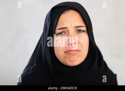 Die junge muslimische Frau in schwarzem Hijab ist über schlechte Nachrichten verärgert und hält ihre Hände dejektiv hoch. Stockfoto