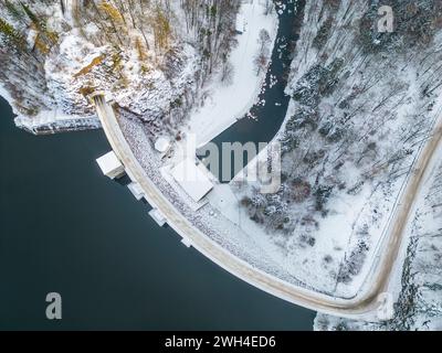 Sek Wasserreservoir mit Betondamm und winterlichen schneebedeckten Hügeln der Iron Mountains herum. Tschechien. Luftaufnahme von der Drohne. Stockfoto