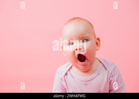 Porträt eines niedlichen kleinen Gähnermädchens, isoliert auf rosa Hintergrund. Ein neugeborenes Baby gähnt und will schlafen Stockfoto