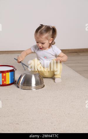 Niedliches kleines Mädchen mit Kochgeschirr und Spielzeugtrommel zu Hause Stockfoto