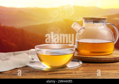 Aromatischer grüner Tee in Glasbecher und Teekanne auf Holztisch in den Bergen Stockfoto