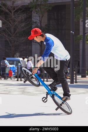 Ein japanischer BMX-Fahrer führt auf einem öffentlichen Platz mitten im Geschäftsviertel in Tokio, Japan, Tricks aus. Stockfoto