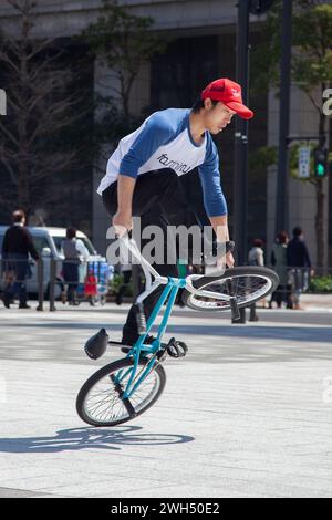 Ein japanischer BMX-Fahrer führt auf einem öffentlichen Platz mitten im Geschäftsviertel in Tokio, Japan, Tricks aus. Stockfoto