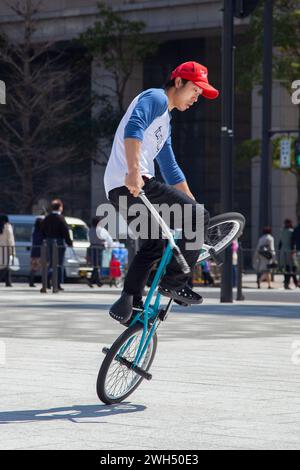 Ein japanischer BMX-Fahrer führt auf einem öffentlichen Platz mitten im Geschäftsviertel in Tokio, Japan, Tricks aus. Stockfoto