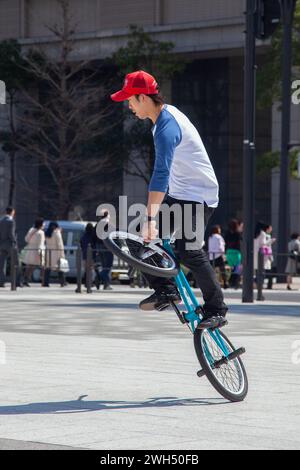 Ein japanischer BMX-Fahrer führt auf einem öffentlichen Platz mitten im Geschäftsviertel in Tokio, Japan, Tricks aus. Stockfoto