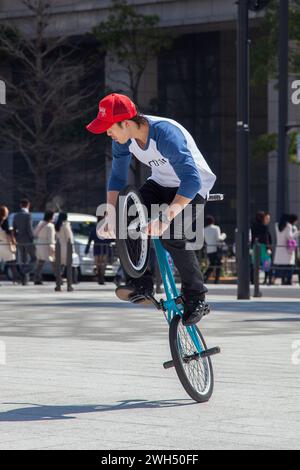 Ein japanischer BMX-Fahrer führt auf einem öffentlichen Platz mitten im Geschäftsviertel in Tokio, Japan, Tricks aus. Stockfoto