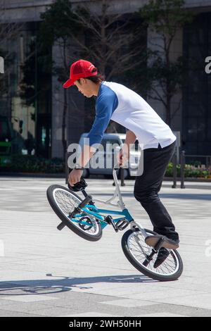 Ein japanischer BMX-Fahrer führt auf einem öffentlichen Platz mitten im Geschäftsviertel in Tokio, Japan, Tricks aus. Stockfoto