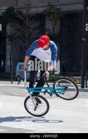 Ein japanischer BMX-Fahrer führt auf einem öffentlichen Platz mitten im Geschäftsviertel in Tokio, Japan, Tricks aus. Stockfoto