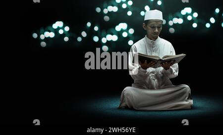 Muslimischer Mann sitzt und liest den koran mit einem unscharfen hellen Hintergrund. Muslimisches Konzept Stockfoto