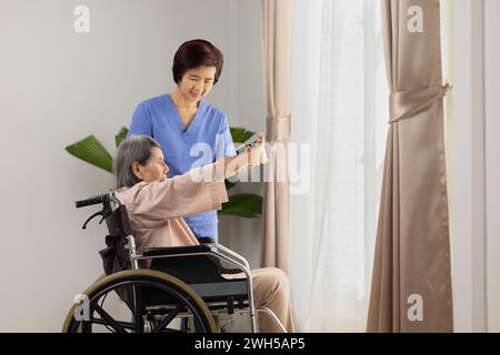 Ältere asiatische Frau, die mit Physiotherapeuten im Wohnzimmer im Rollstuhl Dehnübungen macht. Stockfoto