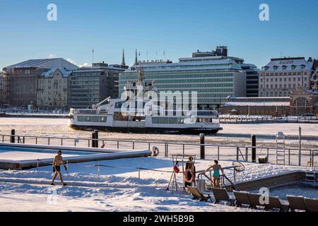 Menschen auf schneebedecktem Allas Sea Pool schwimmende Deck mit Suomenlinna II Fähre im Hintergrund an einem sonnigen Wintertag in Helsinki, Finnland Stockfoto