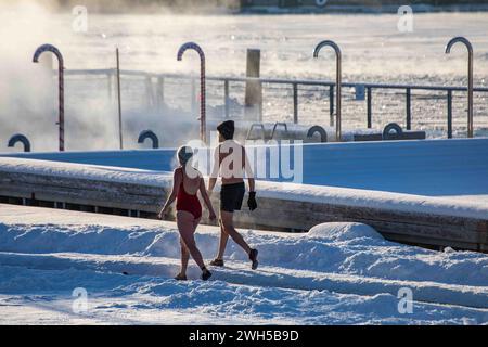 Dampfendes Paar kühlt sich nach der Sauna auf der schneebedeckten Allas Sea Pool Deck an einem kalten Wintertag in Helsinki, Finnland, ab Stockfoto