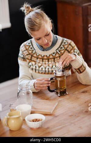 Frau, glücklich und Kräutertee für Ruhe zu Hause und warmes Getränk der Kräuter Mischung für die Gesundheit. Küche, Person und Entgiftung mit trockenen Blättern im Kolben und Stockfoto