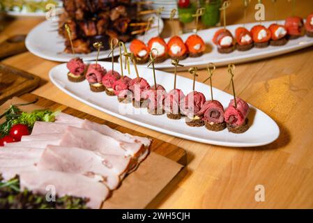 Elegante Canapés mit gerollten Rindfleischscheiben auf Roggenbrot, kunstvoll auf einem Servierteller angeordnet für eine Veranstaltung mit Catering. Stockfoto